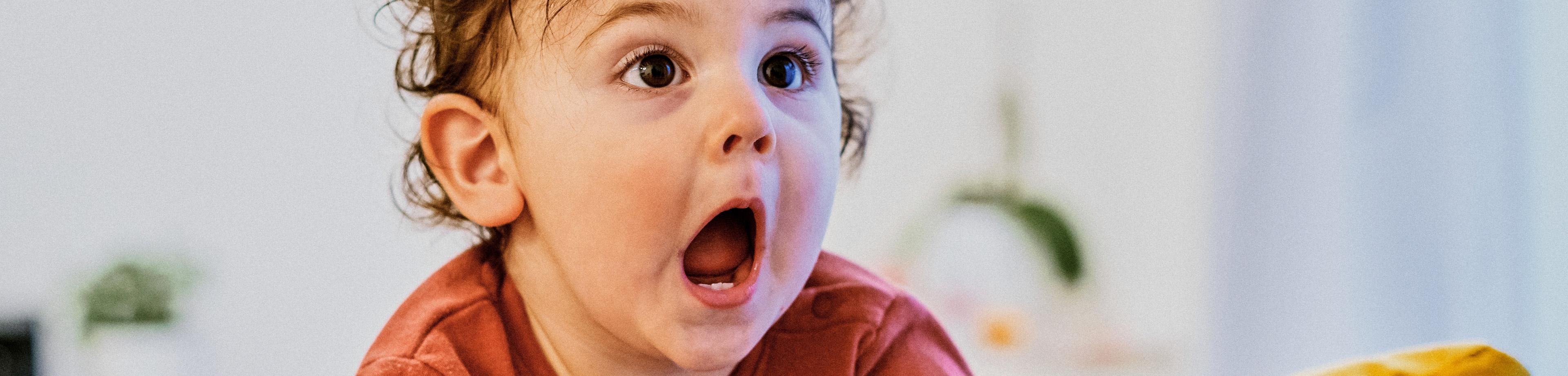Portrait of surprised cute baby sitting on sofa at home