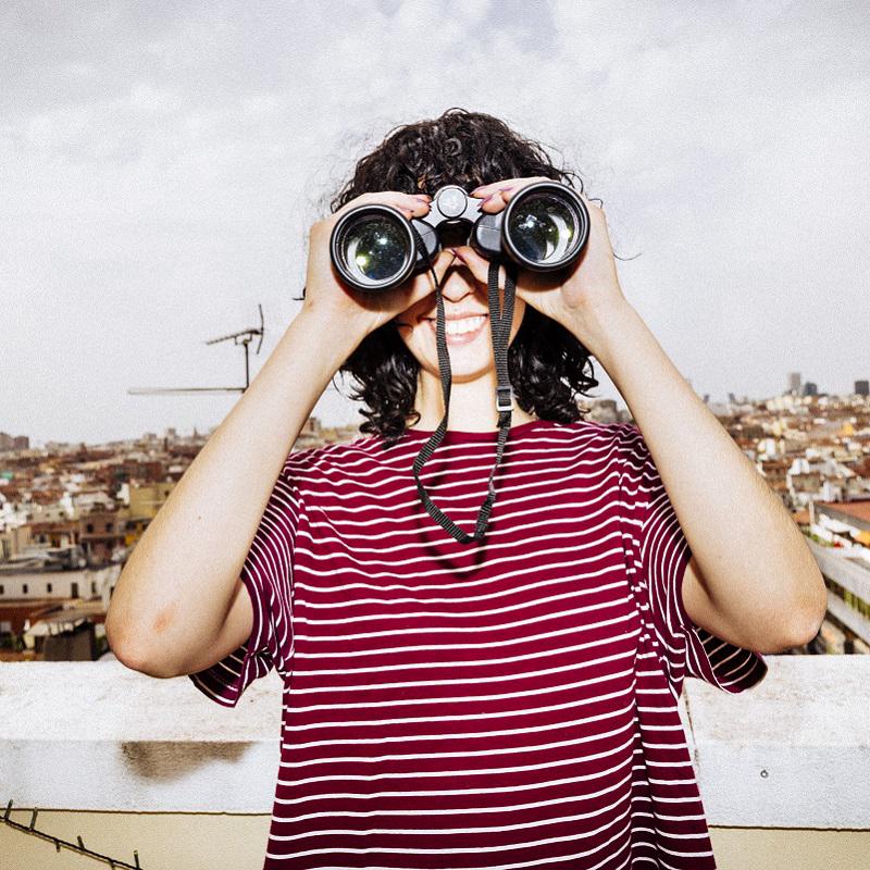 Young woman in striped top looking to camera through binoculars