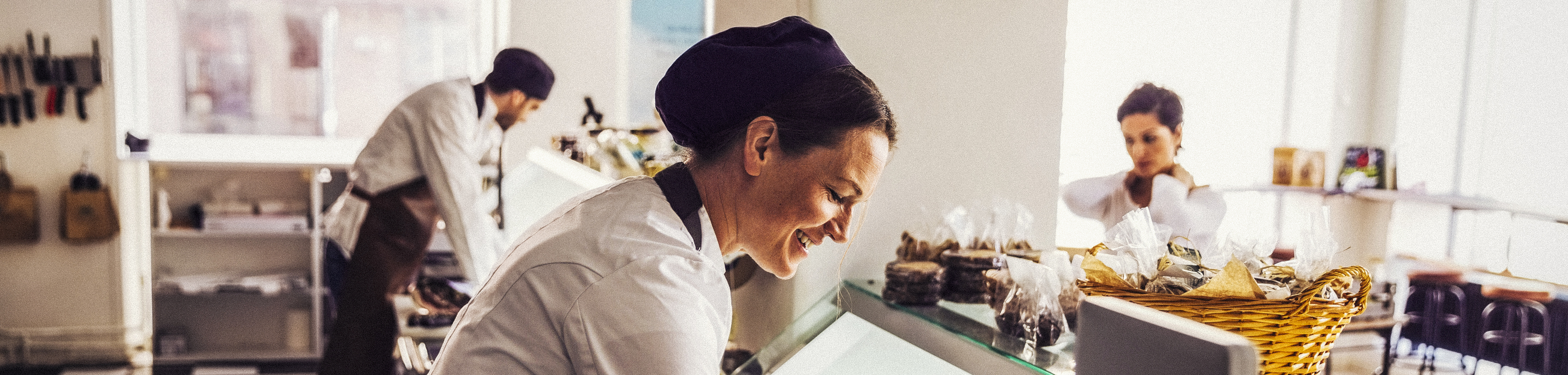 A happy female worker wearing an apron and disposable gloves is standing behind the cafe counter large
