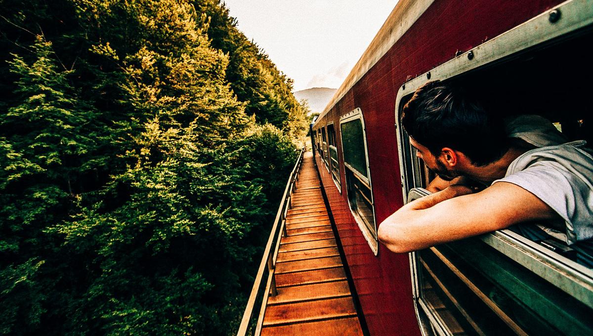 A man hangs outside a train window to look at the scenery during the ride