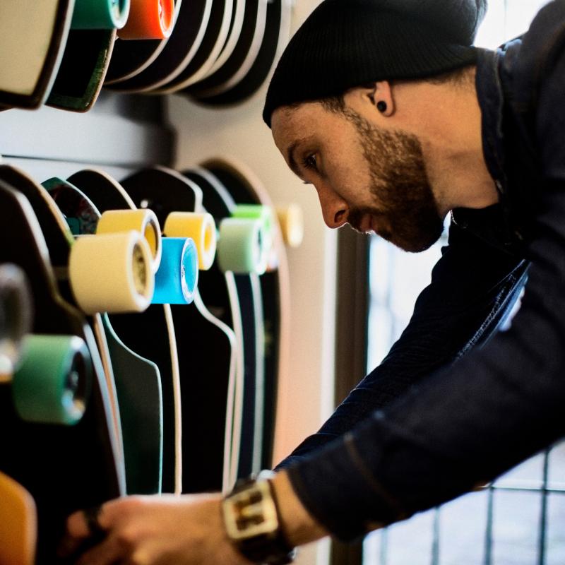 A man in a beanie looks through the longboard selection at a skate store 800