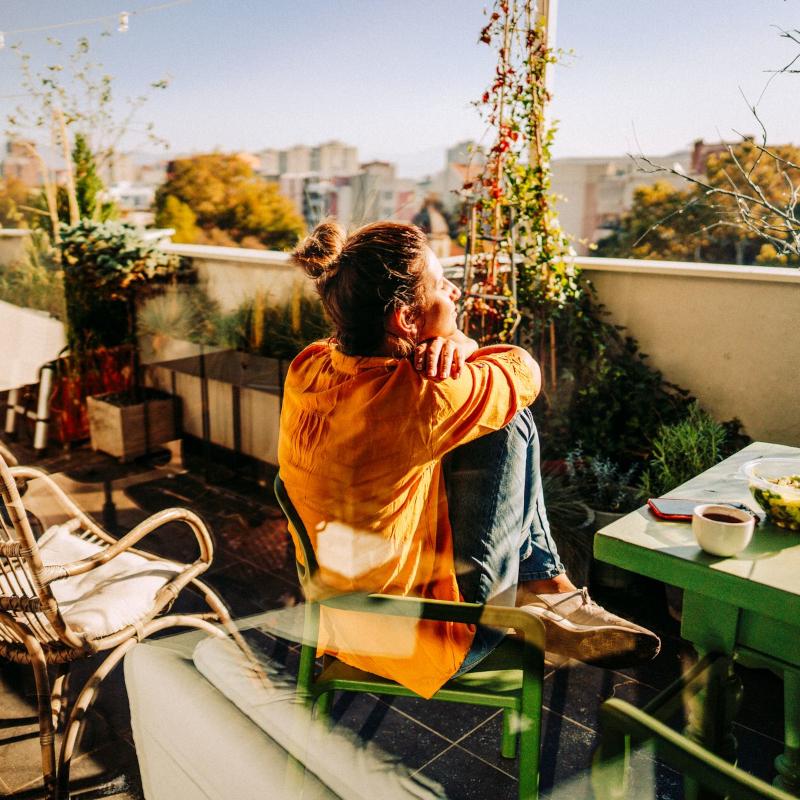 A woman relaxes in the sun on her apartment balcony with her coffee and salad 800