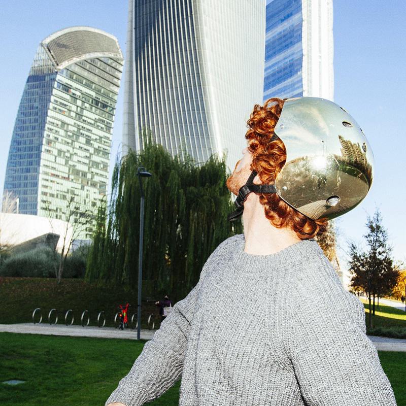 A young man on a scooter looks up at modern city buildings behind him 800x800