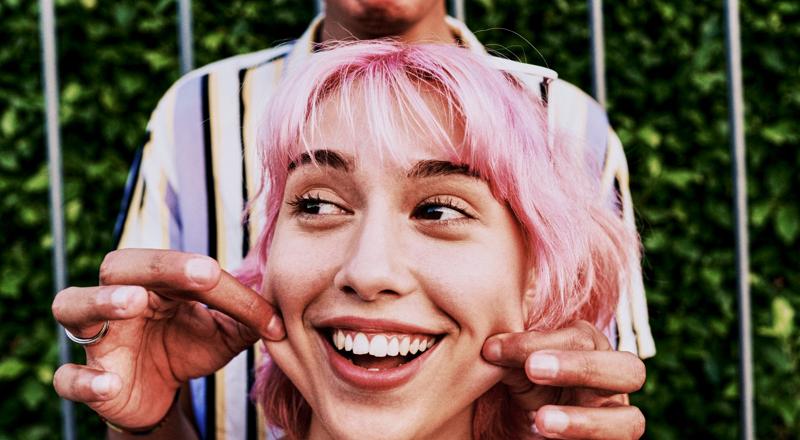 Happy woman with pink hair getting cheeks pinched by friend. Happy woman with pink hair getting cheeks pinched by friend.