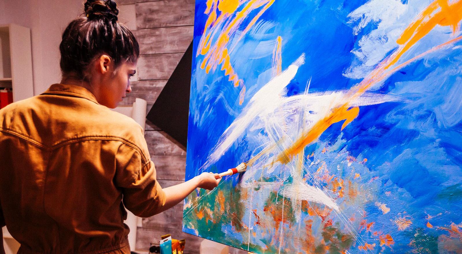 A female artist paints a large canvas on an easel in an art studio