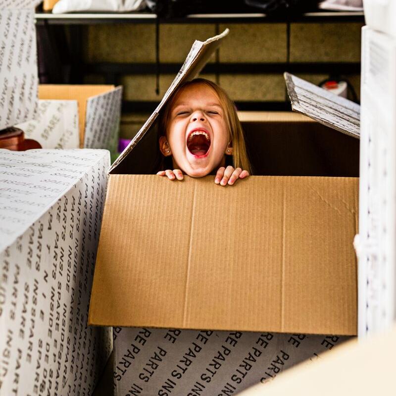 Small child laughing as they hide in a cardboard box indoors focus