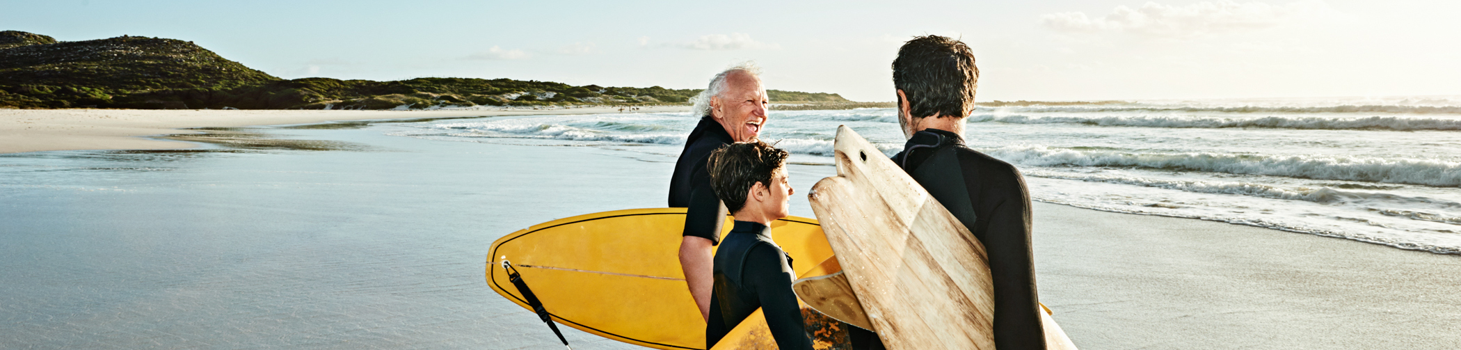 Three people in wetsuits stand in the sea with their surfboards large