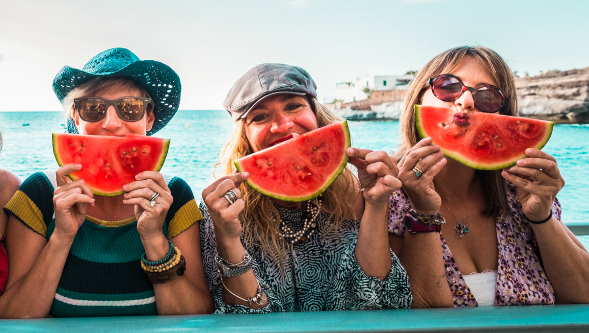 Women on vacation posing for a photo with watermelon slices hero