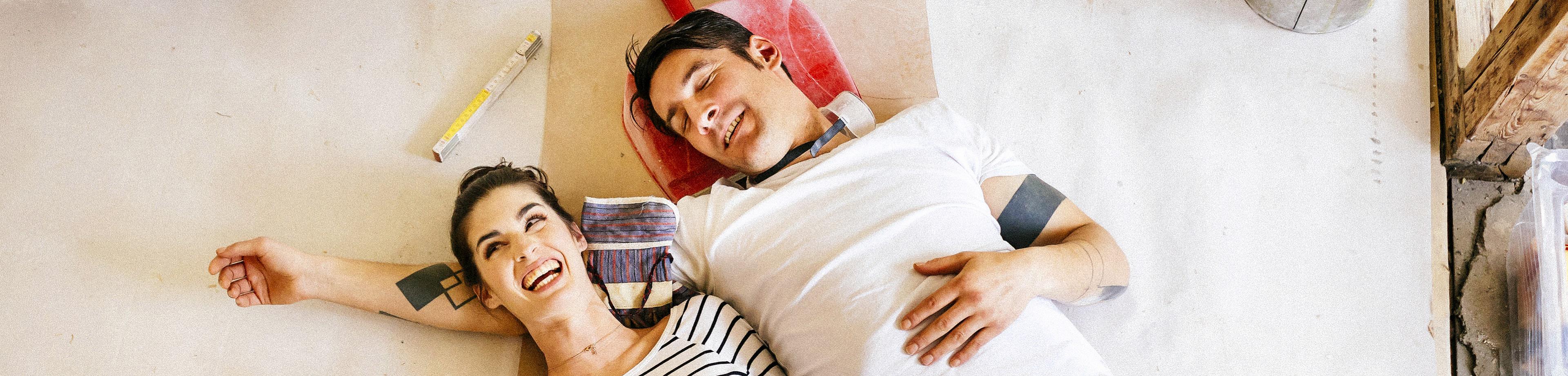 Young couple looking happy laying on the floor of their home renovation project