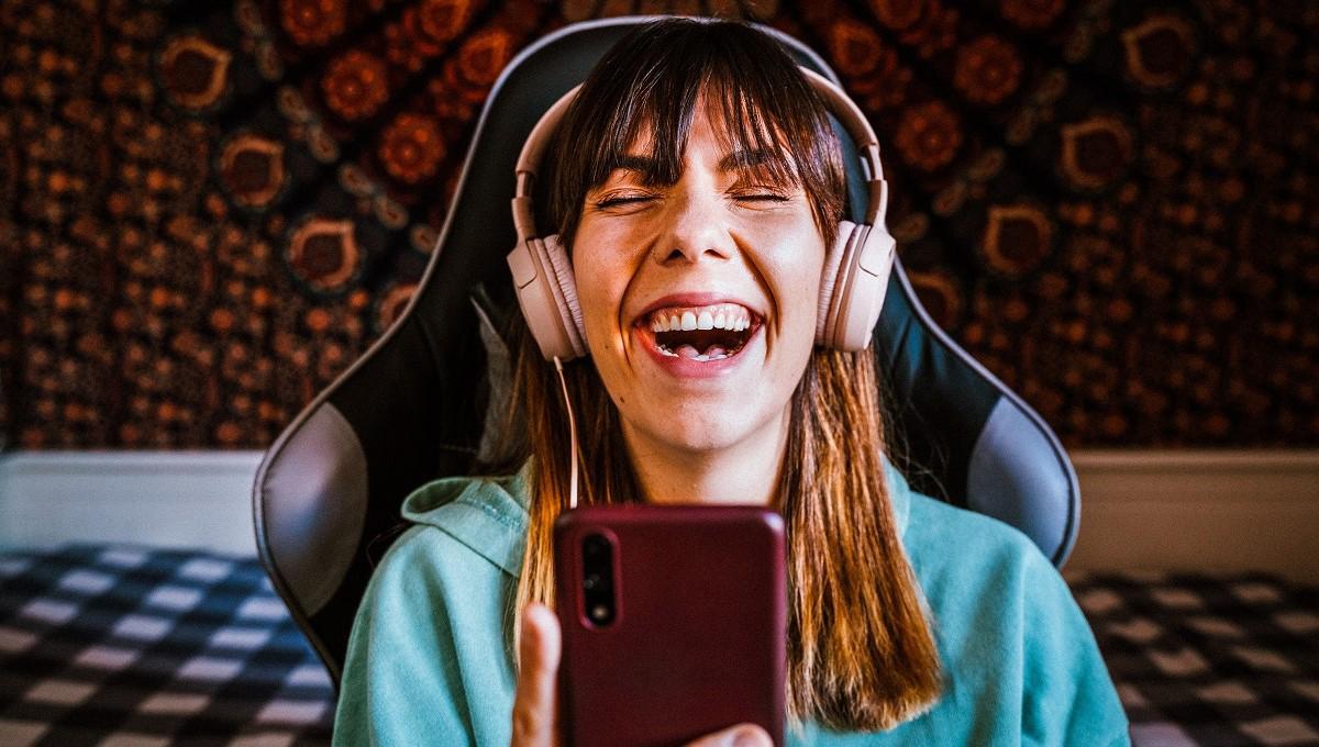 Young woman laughing as she listens to something on headphones and holds her smarphone