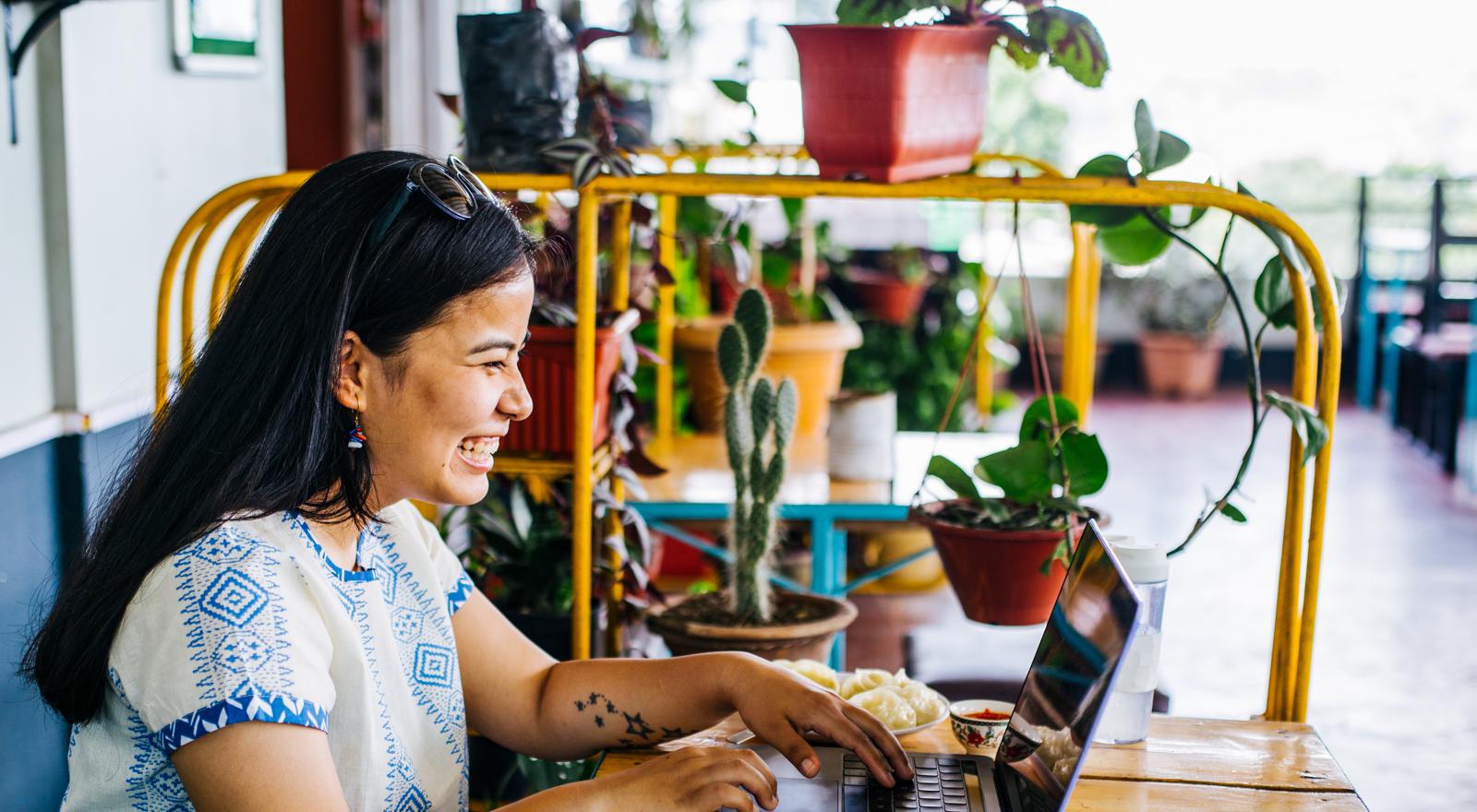 Young woman smiling as she sits outside in a cafe and looks at her laptop